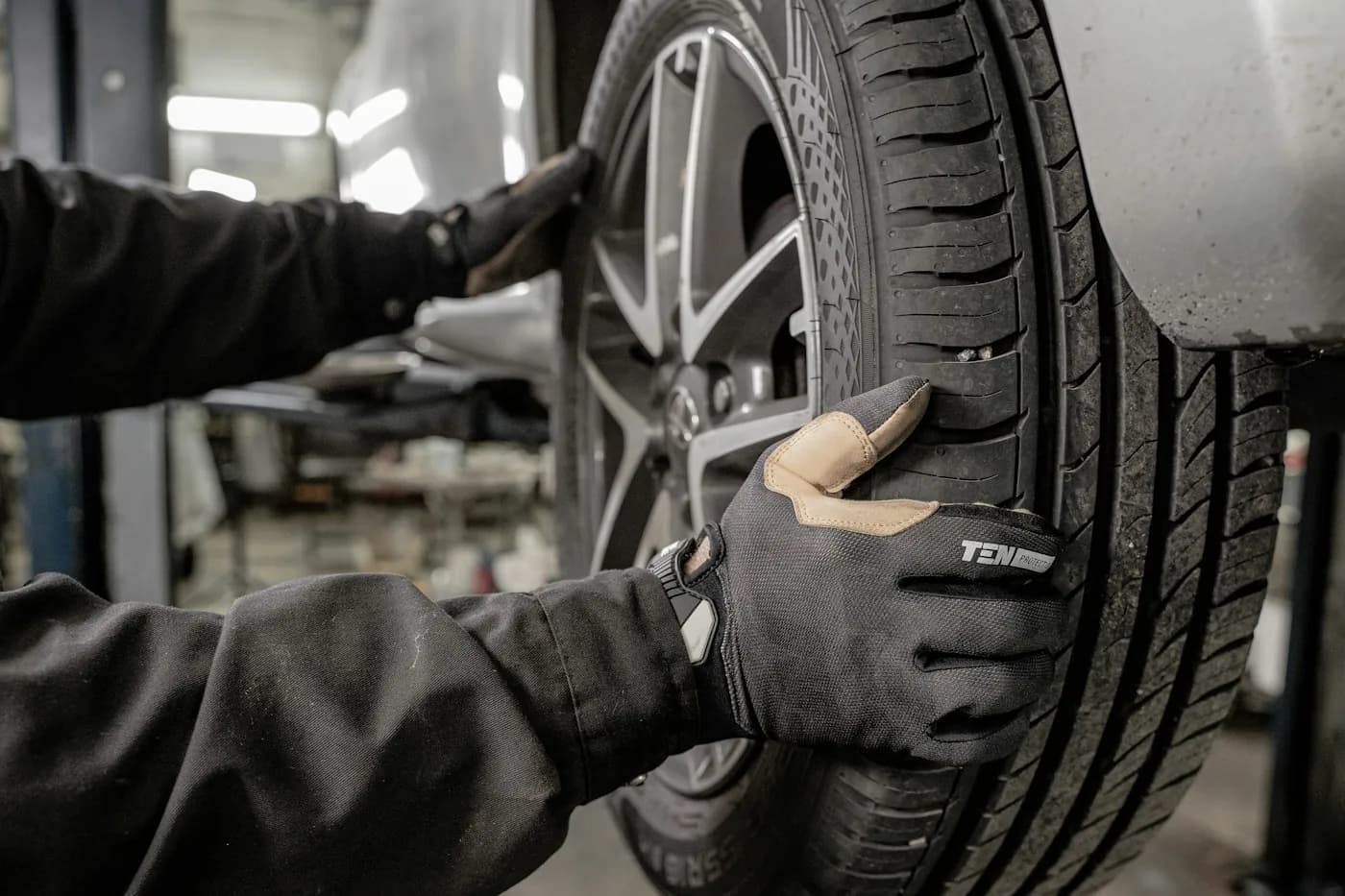 Gloved mechanic handling a vehicle wheel inside a workshop